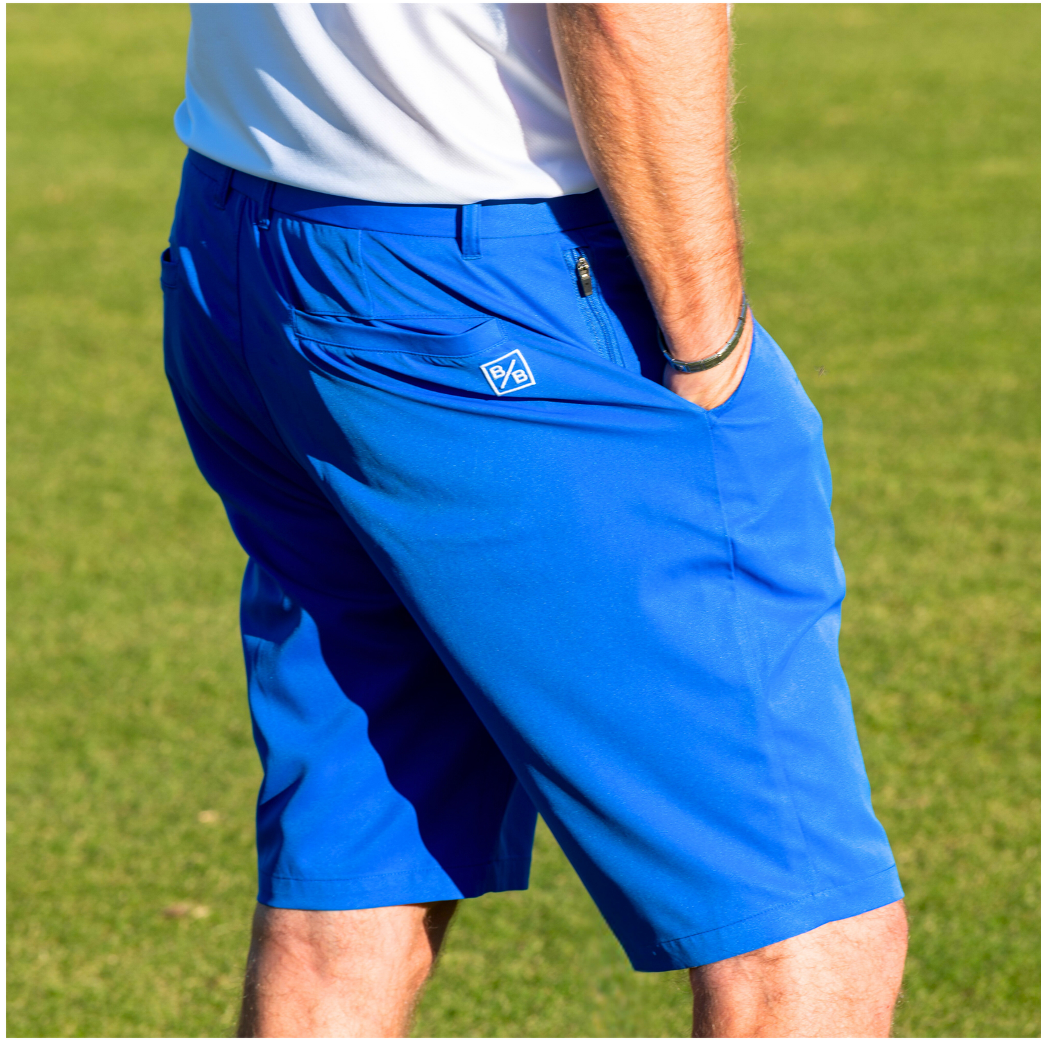 Person wearing blue golf shorts with a logo on a grassy background